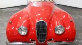 Front view of a restored 1954 Jaguar XK120 with a sleek red paint job